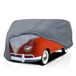 May include: A gray car cover draped over a classic red and white Volkswagen bus. The cover is fitted to the vehicle's shape, protecting it from the elements. The bus has white-walled tires and chrome accents.