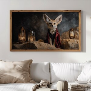 Könnte beinhalten: Ein gerahmtes Kunstwerk mit einem eleganten Fennek-Fuchs, der einen roten Umhang und eine Fliege trägt, vor einem Hintergrund aus Felsen und drei beleuchteten Laternen. Das Kunstwerk hat einen dunklen, stimmungsvollen Hintergrund, der Rahmen ist braun.