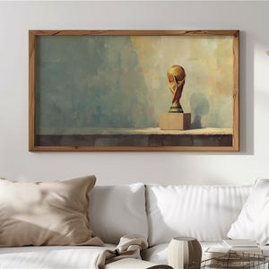 Può includere: Stampa artistica incorniciata raffigurante un trofeo dorato su un piedistallo beige. Lo sfondo è attenuato con sfumature di blu, beige e marrone. La cornice in legno aggiunge un tocco classico all'opera.