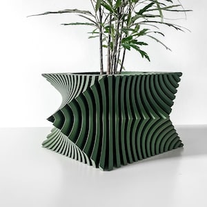 May include: A green, geometric planter with a unique, wave-like design. The planter is filled with a leafy green plant. The planter's dimensions are approximately 12 inches wide and 10 inches tall, making it a stylish addition to any home decor.