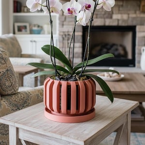 May include: A potted orchid plant with white and purple flowers sits on a light-colored wooden table. The plant is in a coral-colored, slatted planter. The background includes a fireplace, a couch, and a coffee table.