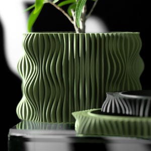 May include: A green planter with a wavy, textured design. The planter is made of a smooth, hard material and has a modern, minimalist style.