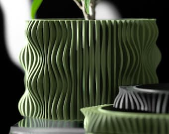 May include: A cylindrical olive green planter with a vertical wavy, ribbed texture containing a small green plant. Next to it sits a smaller, matching olive green circular object with a black center and a similar ribbed exterior design.