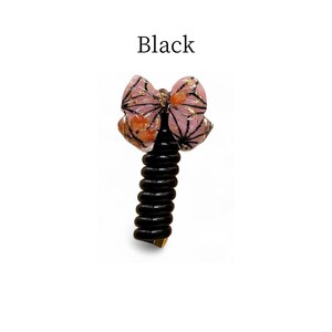 May include: A black bottle stopper with a decorative butterfly design. The butterfly has pink, orange, and gold accents with black outlines. The text "Black" is above the stopper.
