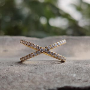 May include: A gold ring with two bands that cross each other. The bands are set with small, clear stones.
