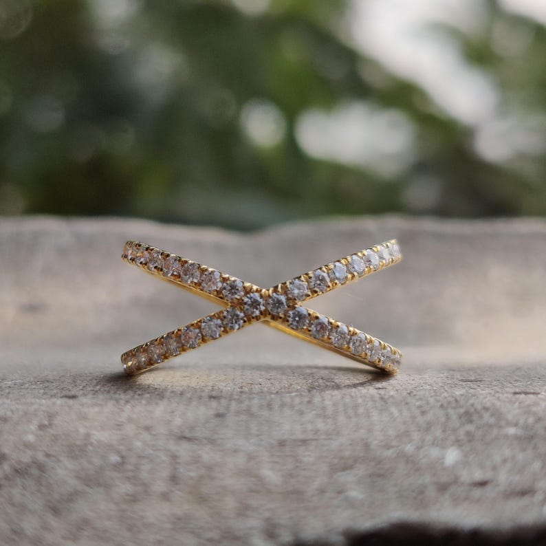 May include: A gold ring with two bands that cross each other. The bands are set with small, clear stones.