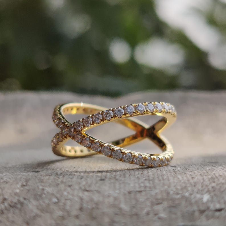 May include: A gold ring with a criss-cross design, set with small clear stones.