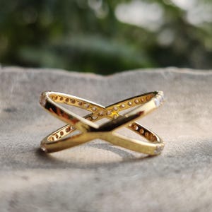 May include: A gold ring with a criss-cross design and small clear stones around the band.