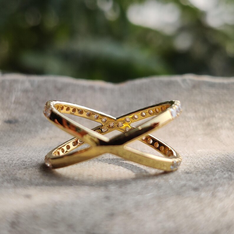 May include: A gold ring with a criss-cross design and small clear stones around the band.