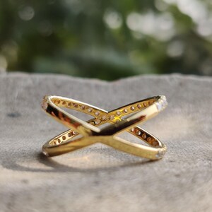 May include: A gold ring with a criss-cross design. The ring is set with small clear stones.