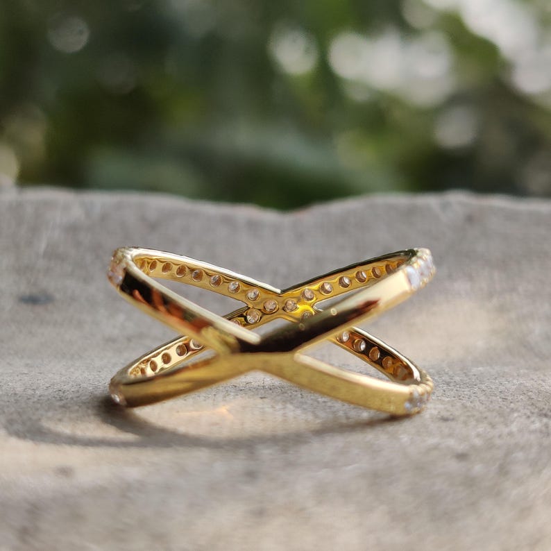 May include: A gold ring with a criss-cross design. The ring is set with small clear stones.