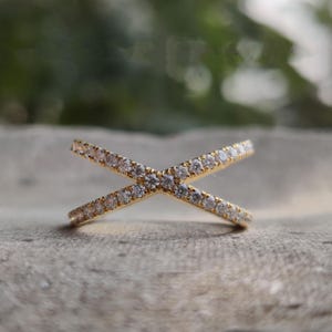 May include: A gold ring with two bands that cross each other. The bands are set with small, clear stones.