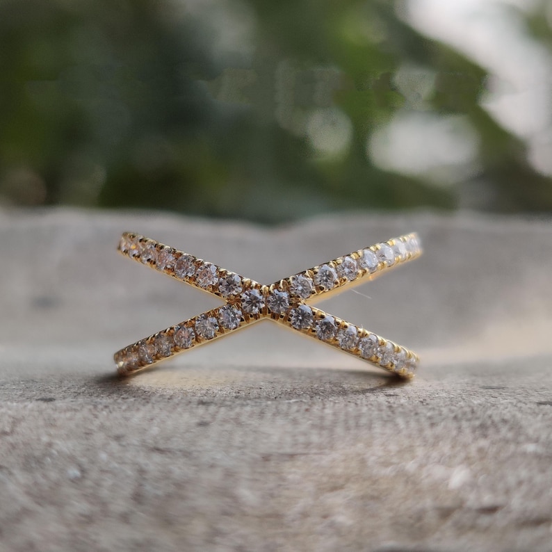 May include: A gold ring with two bands that cross each other. The bands are set with small, clear stones.