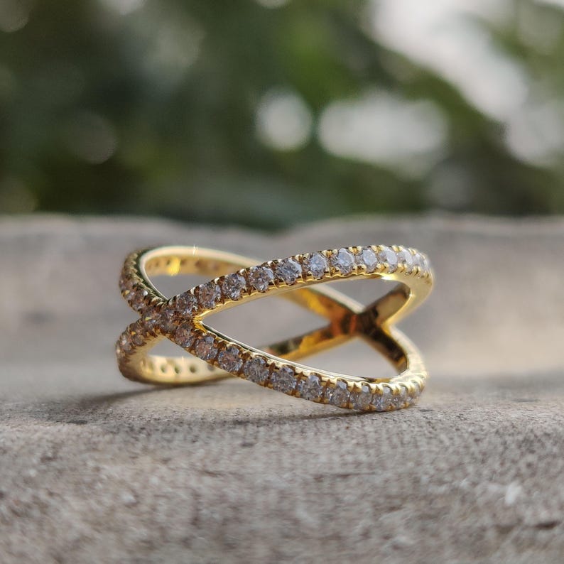 May include: A gold ring with a criss-cross design, set with small clear stones.