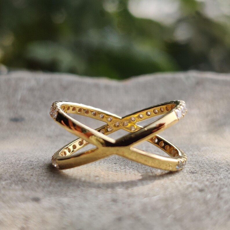 May include: A gold ring with a criss-cross design. The ring is set with small clear stones.