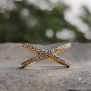 May include: A gold ring with two bands that cross each other. The bands are set with small, clear stones.