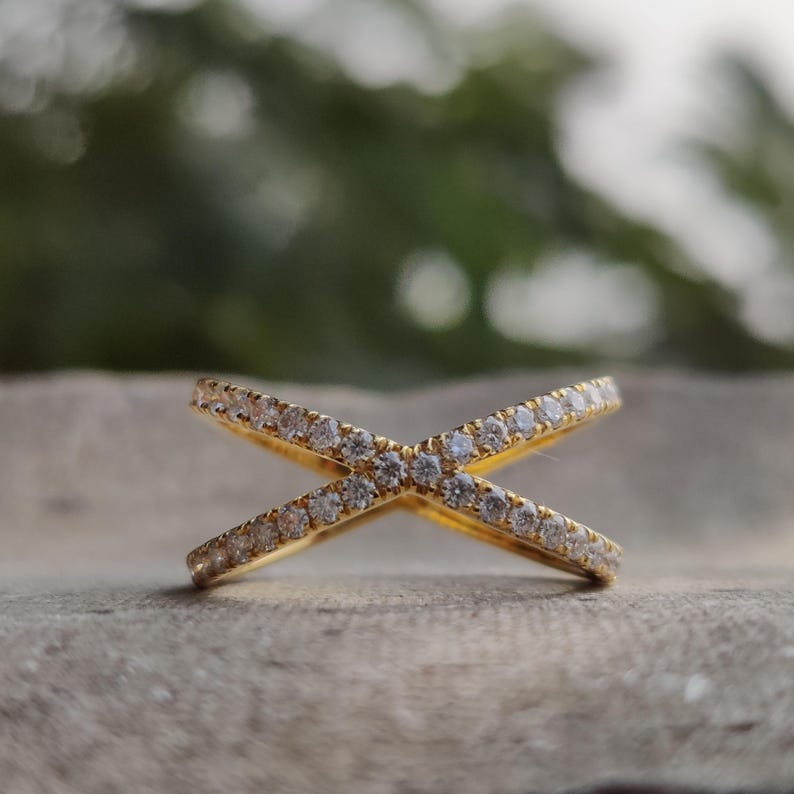 May include: A gold ring with two bands that cross each other. The bands are set with small, clear stones.