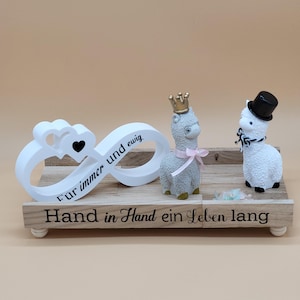 Könnte beinhalten: Holzhochzeitsdekoration mit zwei Lamafiguren, eine mit Krone und die andere mit Zylinder. Ein weißes Unendlichkeitssymbol mit Herzen und Text befindet sich links. Die Basis hat Text.