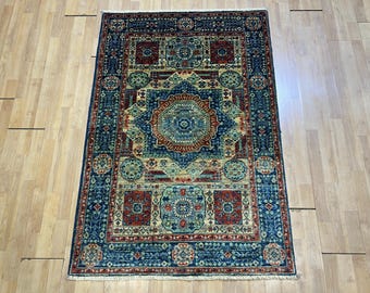 May include: Rectangular area rug with an intricate geometric pattern. The rug features a central medallion in shades of blue, red, and beige, surrounded by a border of repeating floral and geometric motifs. The rug is placed on a light-colored wooden floor.