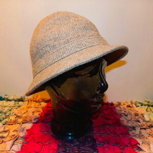May include: A beige felt bucket hat with a wide brim. The hat is sitting on a colorful rug.