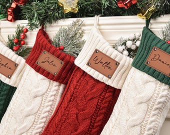以下が含まれることがあります： 緑、赤、クリーム色の4つのパーソナライズされたクリスマスストッキング。それぞれに革製のネームタグが付いています。ストッキングはケーブルニットで、お祝いの緑とオーナメントで飾られており、休日の装飾に最適です。