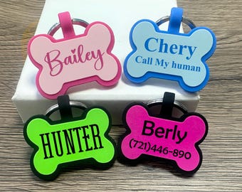 May include: Four colorful bone-shaped dog tags with personalized names and phone numbers. The tags are pink, blue, green, and hot pink. The names on the tags are Bailey, Chery, Hunter, and Berly. The phone number on the hot pink tag is (721) 446-890. The blue tag also has the text "Call My Human".