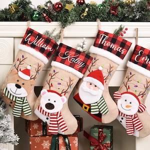 Könnte beinhalten: Vier personalisierte Weihnachtsstrümpfe mit den Namen William, Kathy, Thomas und Emily. Jeder Strumpf hat eine rot-schwarz karierte Manschette und ein festliches Charakterdesign, darunter ein Rentier, ein Eisbär, der Weihnachtsmann und ein Schneemann. Die Strümpfe sind beige.