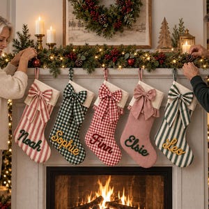 May include: Five hanging Christmas stockings featuring personalised names in cursive script. The stockings include red and white stripes, green and white gingham, red and white gingham, solid dusty rose, and green and white stripes, each with a decorative bow.