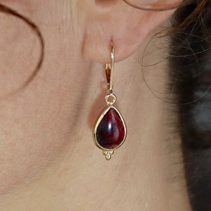Peut inclure: Boucles d'oreilles pendantes en or avec une pierre précieuse rouge en forme de larme.