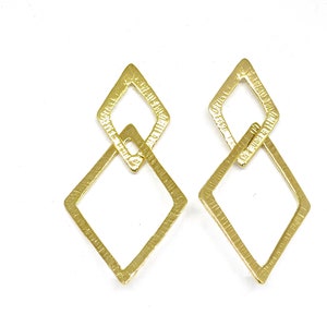 May include: A pair of gold-colored, geometric earrings. Each earring features two textured, diamond-shaped elements linked together. The design is simple yet eye-catching, with a warm, metallic finish. The earrings are presented against a white background.