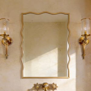 Peut inclure: Un ensemble de vanité de salle de bain comprenant un lavabo en pierre, un miroir doré aux bords ondulés et des appliques murales assorties avec des abat-jours en verre. Le robinet et les appliques ont un motif floral. Le mur est beige clair.