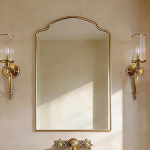 Peut inclure: Un ensemble de salle de bain avec un lavabo en pierre, un miroir doré et des appliques murales assorties. Le lavabo est en pierre naturelle. Le miroir a un sommet en arc. Les appliques ont des abat-jours en verre transparent. Le robinet est doré.