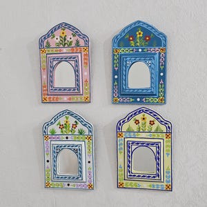 May include: Four decorative mirrors with arched tops and floral designs. Each mirror has a different colour scheme: pink, blue, green, and yellow. The mirrors are adorned with painted floral patterns and a central mirror.