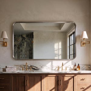 A sleek polished silver rectangle mirror with curved edges bouncing pristine light across a luxurious modern washroom.