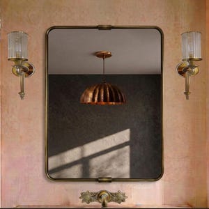 May include: A rectangular wall mirror with a thin bronze frame, flanked by two vertical wall sconces with fluted glass shades. A bronze pendant light with a ribbed dome shade is reflected in the mirror, and a bronze faucet is mounted below.
