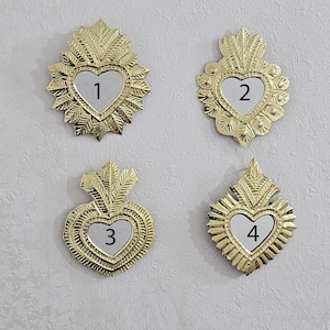 以下が含まれることがあります： 4つの金色のハート型の壁飾り。それぞれに1から4までの数字が入った鏡張りのハートの中心があります。装飾は、精巧な葉のようなデザインに囲まれ、明るい灰色の壁に取り付けられています。