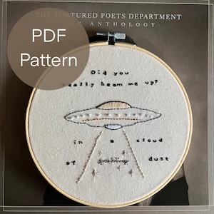 May include: An embroidered UFO design on a cream-colored fabric, set within a wooden embroidery hoop. The text "Did you really beam me up?" and "in a cloud of sparkling dust" are stitched around the UFO. The words "PDF Pattern" are also visible.