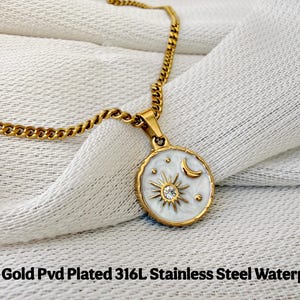 May include: A gold-colored chain necklace with a round pendant featuring a white enamel inlay, a gold sunburst design with a central clear stone, and a gold crescent moon. The text 18K Gold Pvd Plated 316L Stainless Steel Waterproof is visible.