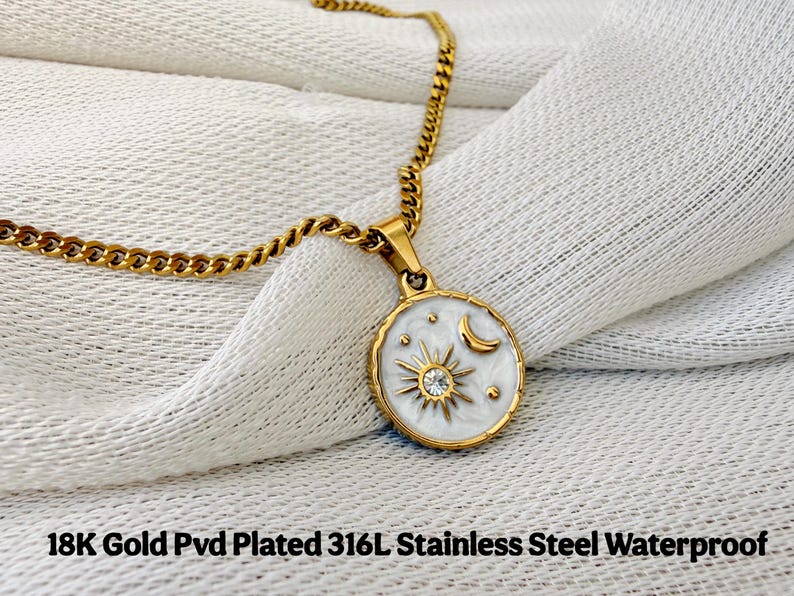May include: A gold-colored chain necklace with a round pendant featuring a white enamel inlay, a gold sunburst design with a central clear stone, and a gold crescent moon. The text 18K Gold Pvd Plated 316L Stainless Steel Waterproof is visible.