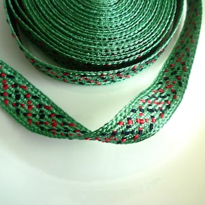 May include: Green ribbon with red and black woven details. The ribbon is rolled up and laid out flat.