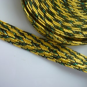May include: A close-up of gold and black trim with green accents. The trim is woven and has a shiny finish.