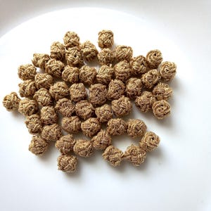 May include: A collection of small, round, gold-colored fabric buttons featuring a woven knot design. Each button is constructed from metallic thread, creating a textured, spherical appearance with a consistent, shimmering finish throughout.