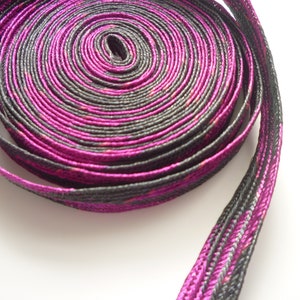 May include: A close-up of a roll of black and magenta ribbon with a subtle shimmer. The ribbon is rolled up tightly and the edges are visible.
