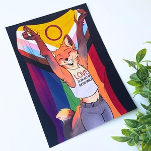 May include: A rectangular art print featuring an anthropomorphic fox with orange fur, wearing a white tank top with the text LOVE IS AN ACT OF RESISTANCE, holding a large intersex-inclusive pride flag with yellow, white, purple, and rainbow stripes.