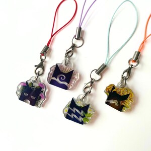 May include: Four acrylic charms featuring stylized cat head silhouettes with internal floral and abstract patterns. Each charm is attached to a metal lobster clasp and a colorful nylon cord in red, lavender, light blue, and orange, respectively.