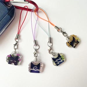 May include: Four small acrylic charms attached to colorful nylon cords with silver-toned lobster clasps. Each charm features a unique dark silhouette shape layered over pressed floral designs in shades of purple, blue, green, and yellow.