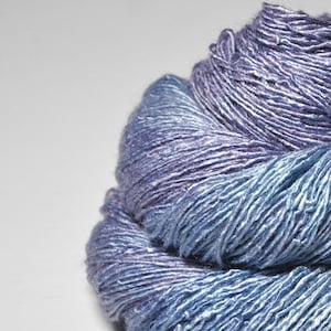 May include: A skein of blue and purple silk yarn. The yarn is soft and lustrous, with a subtle sheen.