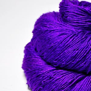 May include: A close-up of a skein of vibrant purple yarn. The yarn is tightly wound, revealing the texture of the fibers. The rich color and soft appearance suggest it is suitable for knitting or crocheting projects. The yarn is against a white background.