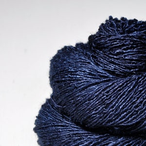 May include: A skein of deep blue yarn with a subtle sheen. The yarn is tightly wound and has a textured surface.