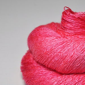 May include: A skein of bright pink yarn, made of silk, is wound into a ball shape.